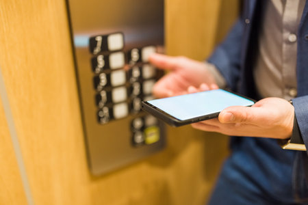 Man hands holding blank screen mobile phone while using elevator control panel.