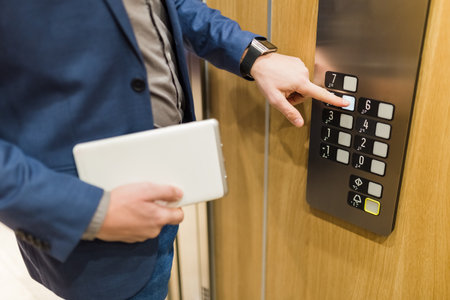 Man holding digital tablet while using elevator control panel.の写真素材