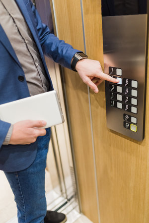 Close up of businessman with tablet device pressing elevator button. Business and office building...