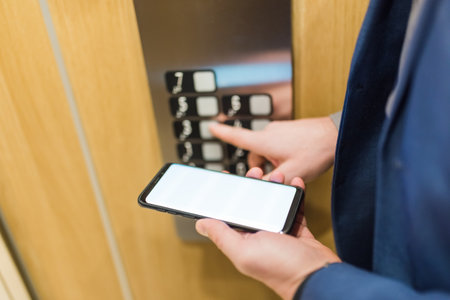 Man hands holding blank screen mobile phone while using elevator control panel.