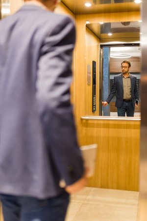 Businessman with digital tablet entering modern wooden elevator.