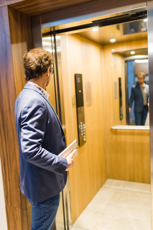 Modern man holding tablet device and using elevator in office building.の写真素材