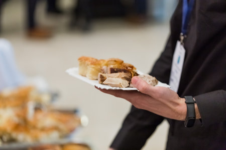 Close up of man hand holding plate and scooping food at buffet table catering in hotel or restaurant business conference.の写真素材
