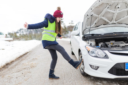 Angry woman kicking her broken car at roadside. Winter scene.の写真素材