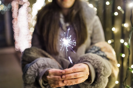 Woman holding burning bengal in New Year eve with Christmas lights in the background.の写真素材