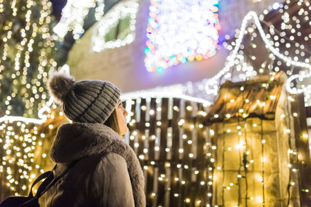 Young woman standing in front of house decorated with christmas lights.の写真素材