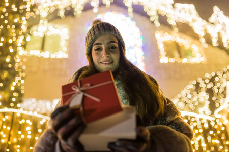 Beautiful young woman opening gift box outdoors. Christmas new year surprise concept.の写真素材