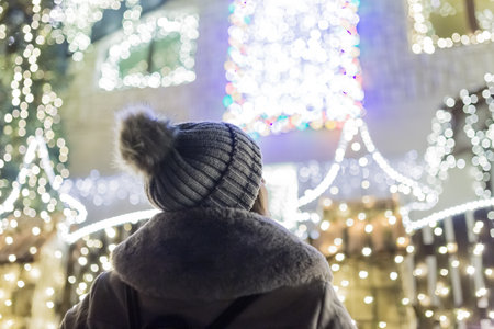Rear view of fashionable female enjoying christmas spirit in front of house with beautiful holiday decoration.の写真素材