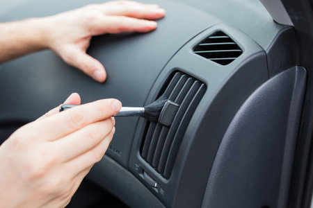 Man hands using cleaning brush and removing dust from car air conditioning vent grill. Car detailing or valeting concept.の写真素材