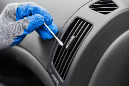 Car service professional holding cotton swab and removing dust from air conditioning vent grilleの写真素材