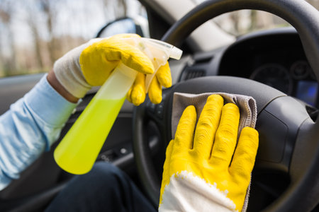 Worker cleaning car steering wheel with microfiber cloth and holding spray bottle of disinfectant.の写真素材