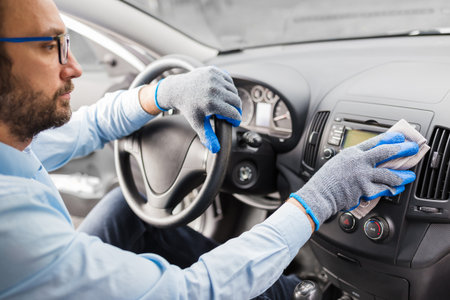 Man with protective gloves cleaning car dashboard with microfiber cloth.の写真素材
