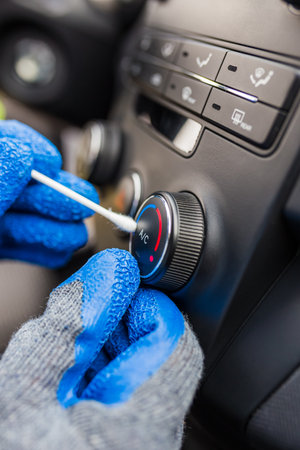 Car service professional holding cotton swab and removing dust from air conditioner button.の写真素材