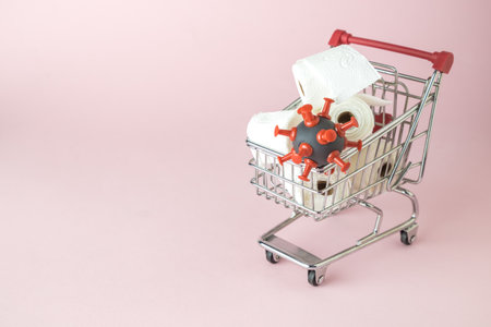 Consumer panic corona virus concept. Toilet paper rolls and coronavirus cell in shopping cart abstract on pastel pink background.の写真素材