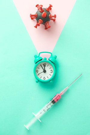 Time is running out. Coronavirus cure vaccine minimal creative concept made of covid-19 cell symbol, alarm clock and syringe.の写真素材