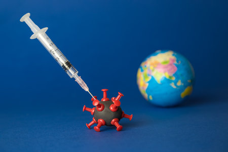 Covid-19 vaccination abstract made of syringe, virus cell model and earth globe against dark blue background.の写真素材