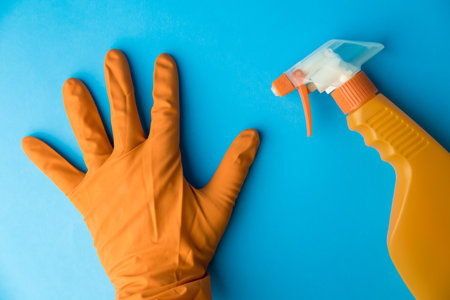 Flat lay of spray bottle of disinfectant and hand in protective glove against blue background minimal creative cleaning concept.の写真素材