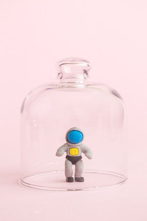 Spaceman in isolation from covid-19 under glass cover abstract against pastel pink background.の写真素材