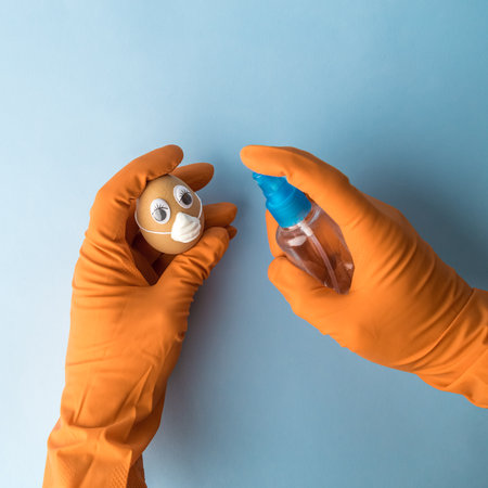 Easter disinfection abstract made of hand wearing gloves and using disinfectant spray to disinfect egg with protective medical mask.の写真素材