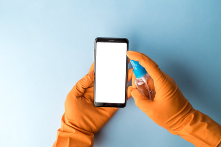 Hands wearing protective rubber gloves spraying alcohol, disinfectant spray on blank screen mobile phone, prevent infection of Covid-19 virus,contamination of germs or bacteria, wipe or cleaning phone to eliminate,outbreak of Coronavirusの写真素材