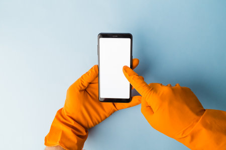Flat lay of hands wearing protective rubber gloves holding and using smartphone touchscreen, coronavirus protection concept.の写真素材