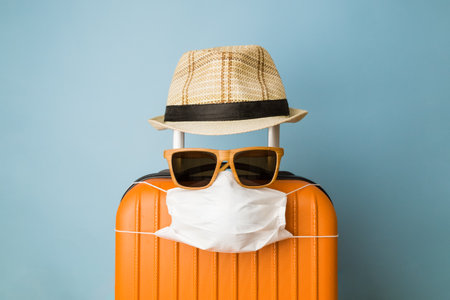 Travel restriction abstract made of tourist in form of of luggage with face mask, sunglasses and hat.の写真素材