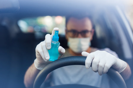 Portrait of driver with face mask and medical gloves holding disinfectant spray bottle, coronavirus...