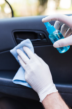 Man hands in protective gloves cleaning car interior door by using microfiber cloth and bottle of spray disinfectant.の写真素材