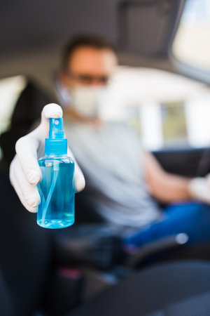 Man driver in protective mask with hands wearing rubber gloves holding alcohol sanitizer sprayer, covid-19 protection from bacteria and virus infection. Car interior.の写真素材