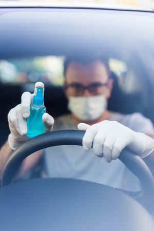 Close up of driver in protective mask with hands wearing rubber gloves on steering wheel holding alcohol sanitizer sprayer, covid-19 protection from bacteria and virus infection.の写真素材