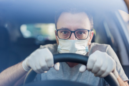 Close up of driver in protective mask with hands in rubber gloves on steering wheel, covid-19 protection from bacteria and virus infection.の写真素材