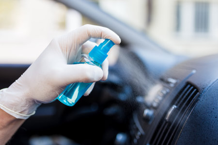 Hand in medical glove holding sanitizer spray bottle and disinfecting air conditioner air grille.の写真素材