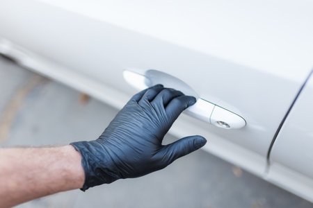 Hand wearing medical rubber gloves holding car door handle.の写真素材