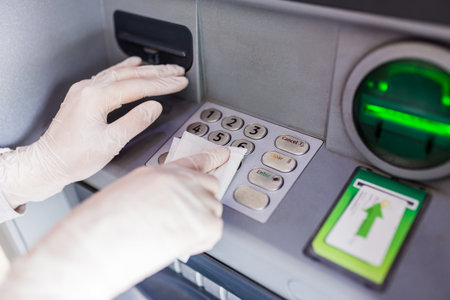 Close up of hands wearing protective medical gloves cleaning numeric atm keyboard with wet wipe. Public disinfection and coronavirus pandemic.の写真素材