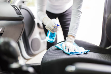 Woman with protective gloves cleaning car seat with microfiber cloth and spray bottle disinfectant.の写真素材