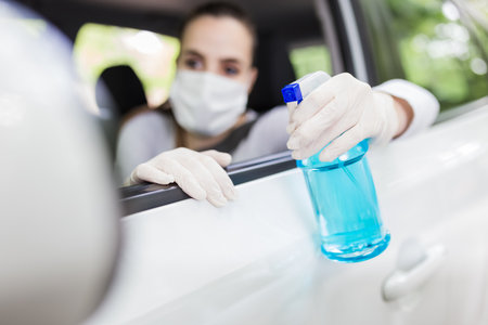 Portrait of woman with surgical mask sitting in car and holding sprayer sanitizer. Hygiene concept.の写真素材