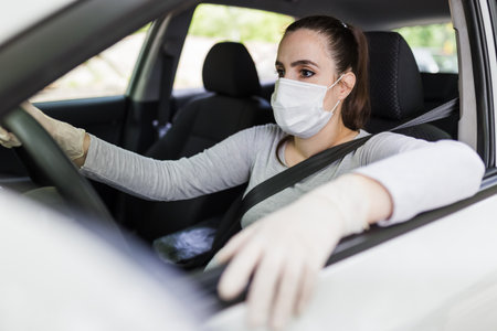 Close up of female driver in protective mask with hands in rubber gloves on steering wheel, covid-19 protection from bacteria and virus infection.の写真素材