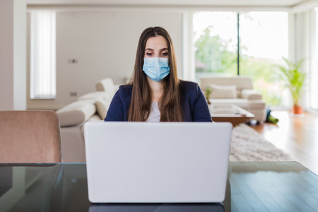 Young business woman working from home on laptop and wearing protective mask. Coronavirus quarantine concept.の写真素材