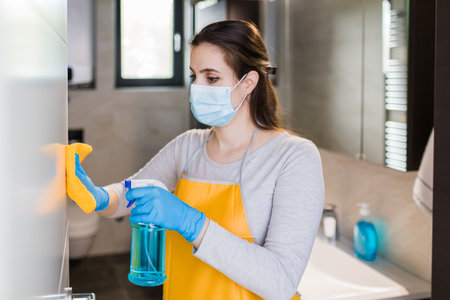 Woman housekeeper wipes the door with rag and using spray disinfectant.の写真素材