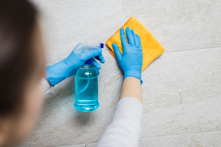 Young woman cleaning ceramic tiles with rag and spray disinfectant in bathroom.の写真素材