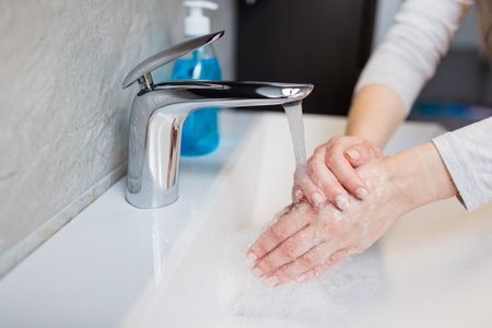 Washing hands under the water tap or faucet without soap. Hygiene concept detail. Beautiful hand and water stream in bathroom. New modern basin cleaning.の写真素材