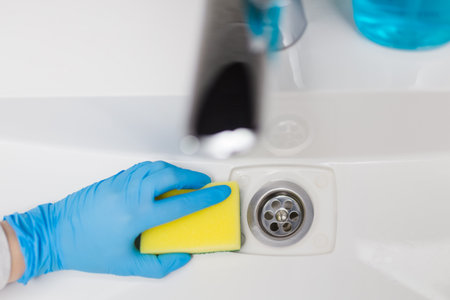 Woman hand in blue protective glove using sponge to clean basin sink in bathroom.の写真素材