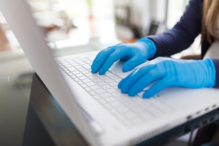 Close up of female hands in surgical gloves on laptop keyboard. Work from home covid-19 concept.の写真素材