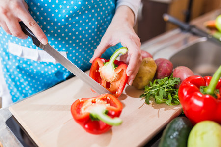 Close up of woman cutting red paprika pepper on cutting board in the kitchen.の写真素材