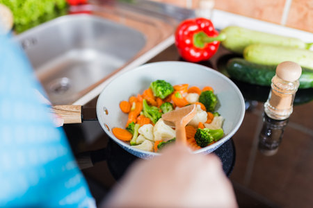 Woman cooking vegetables in frying pan on electric stove.の写真素材