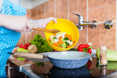 Woman adding mixed vegetables in pan. Vegetarian food preparation and cooking concept.の写真素材