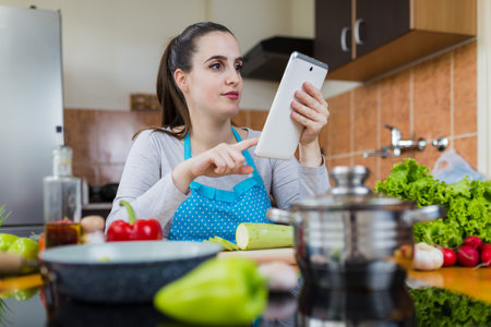 Woman using digital tablet in kitchen to find healthy meal recipe on the internet.の写真素材