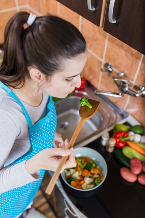 Woman tasting food while preparing homemade vegetarian meal.の写真素材