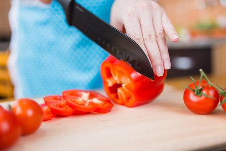 Close up of woman in apron slicing bell pepper on cutting board in kitchen. Healthy meal preparation concept.の写真素材
