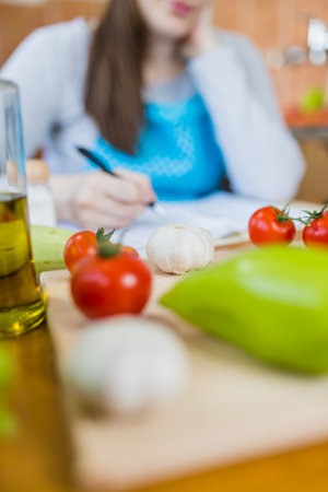 Close up of woman in apron sitting at kitchen table and writing vegetable meal recipe.の写真素材